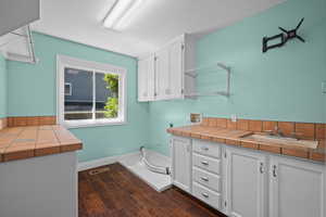 Laundry room with hookup for a washing machine, a textured ceiling, electric dryer hookup, cabinet space, and dark wood-style flooring
