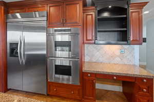 Kitchen featuring appliances with stainless steel finishes, light stone countertops, decorative backsplash, and brown cabinetry