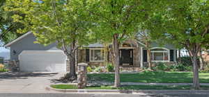 View of property hidden behind natural elements with stone siding, driveway, a garage, and a front lawn