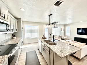 Kitchen featuring light stone counters, a kitchen island with sink, pendant lighting, stainless steel appliances, and light wood-style floors