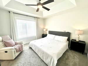 Carpeted bedroom with a raised ceiling and ceiling fan