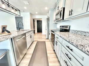 Kitchen featuring appliances with stainless steel finishes, light stone counters, a textured ceiling, light wood-style floors, and hanging light fixtures