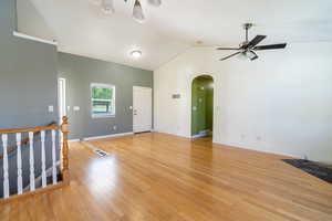Empty room with lofted ceiling, light wood-type flooring, and arched walkways