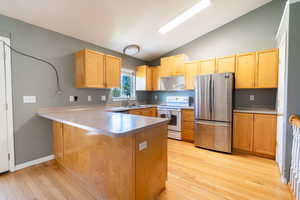 Kitchen with freestanding refrigerator, lofted ceiling, white electric range, light wood-type flooring, and light countertops