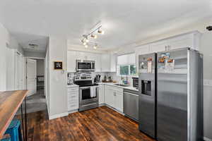 Kitchen featuring stainless steel appliances, decorative backsplash, white cabinets, dark wood-style floors, and wooden counters