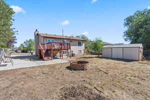 Back of property featuring stairway, an outdoor fire pit, a wooden deck, a storage shed, and a patio