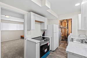 Kitchen with electric stove, light countertops, white cabinets, and freestanding refrigerator