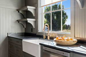 Kitchen featuring open shelves, dishwasher, gray cabinetry, and dark stone countertops