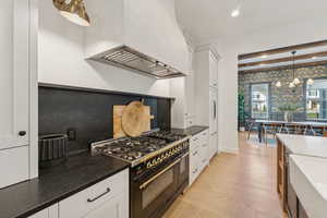 Kitchen with white cabinets, pendant lighting, double oven range, dark stone countertops, and beamed ceiling