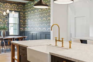 Kitchen featuring wainscoting, wallpapered walls, a decorative wall, light stone countertops, and light wood-style flooring