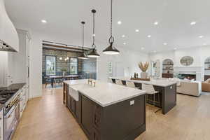 Kitchen with open floor plan, decorative light fixtures, a warm lit fireplace, light stone counters, and double oven range