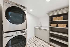 Laundry room featuring recessed lighting, stacked washing machine and dryer, and cabinet space