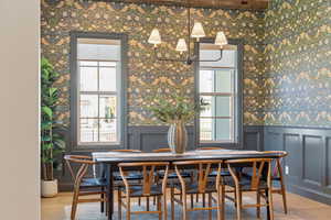 Dining room featuring wallpapered walls, wood finished floors, a wainscoted wall, and a decorative wall