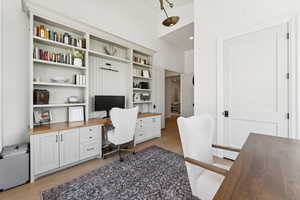 Home office featuring light wood finished floors, built in desk, and a high ceiling
