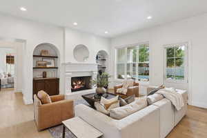 Living area with recessed lighting, light wood finished floors, built in features, and a warm lit fireplace