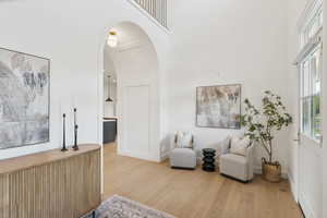 Sitting room with arched walkways, light wood-type flooring, and a high ceiling