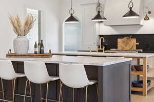 Kitchen featuring a breakfast bar, hanging light fixtures, light stone countertops, and gray cabinetry