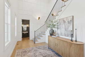 Foyer featuring stairway, light wood-style flooring, plenty of natural light, and a high ceiling
