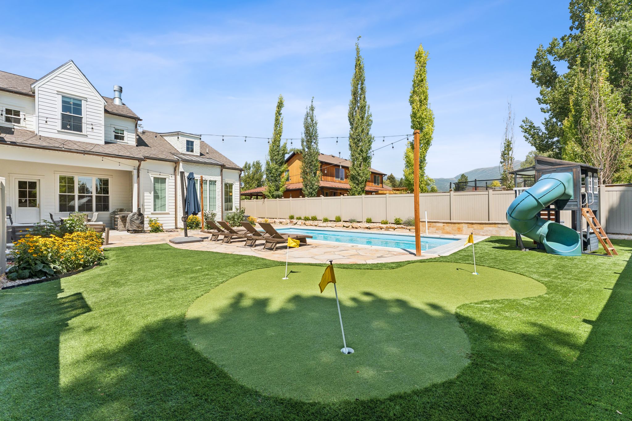 View of swimming pool featuring a patio, an area to practice putting, a fenced backyard, a playground, and a water slide