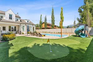 View of swimming pool featuring a patio, an area to practice putting, a fenced backyard, a playground, and a water slide