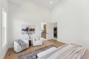 Bedroom featuring ensuite bath, high vaulted ceiling, light wood-type flooring, stacked washer / drying machine, and recessed lighting
