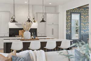 Kitchen with wainscoting, white cabinetry, a breakfast bar, light stone counters, and a center island with sink