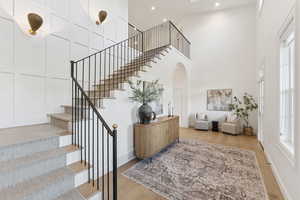 Staircase with a towering ceiling, wood finished floors, arched walkways, and a decorative wall