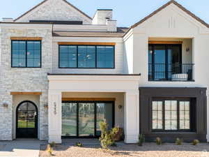 View of front of house with a balcony, stone siding, a chimney, and stucco siding