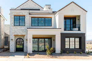 View of front facade featuring stone siding, a balcony, stucco siding, and a chimney