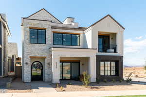 View of front of home with stone siding, a balcony, a chimney, and stucco siding