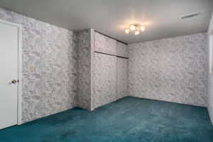Unfurnished bedroom with dark carpet, wallpapered walls, and a textured ceiling