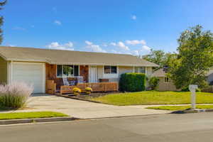 Ranch-style house with an attached garage, roof with shingles, driveway, and front yard
