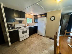 Kitchen with dark cabinets, white appliances, light countertops, and under cabinet range hood