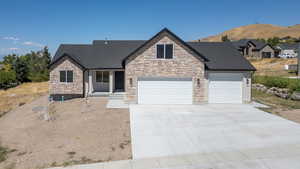 View of front of property featuring a garage, covered porch, stone siding, driveway, and roof with shingles