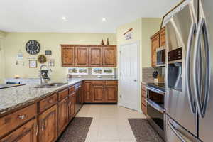 Kitchen featuring appliances with stainless steel finishes, tasteful backsplash, light stone countertops, brown cabinetry, and recessed lighting