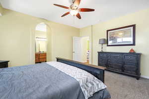 Bedroom with carpet, ceiling fan, connected bathroom, and arched walkways