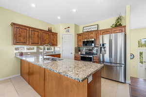 Kitchen with appliances with stainless steel finishes, decorative backsplash, a peninsula, light stone counters, and brown cabinets