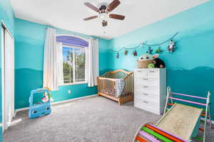 Carpeted bedroom with a ceiling fan and a crib