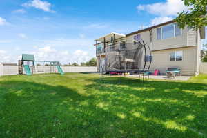 Fenced backyard featuring a trampoline, a balcony, a patio, and a playground