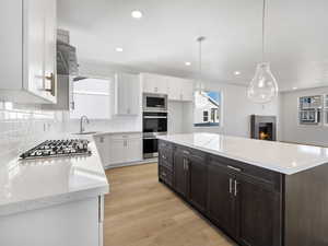 Kitchen with white cabinets, light wood-style floors, light stone counters, a center island, and recessed lighting