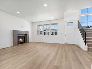 Unfurnished living room with stairway, recessed lighting, a glass covered fireplace, and light wood-type flooring