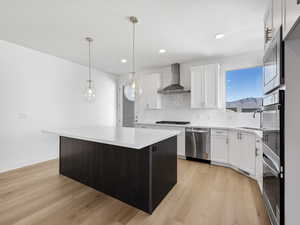 Kitchen with a kitchen island, backsplash, white cabinetry, stainless steel appliances, and pendant lighting