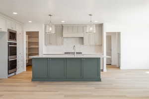 Kitchen featuring an island with sink, light wood-style flooring, backsplash, decorative light fixtures, and recessed lighting