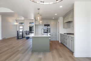 Kitchen with gray cabinetry, a chandelier, a kitchen island with sink, light wood-type flooring, and recessed lighting