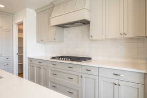 Kitchen with premium range hood, light stone countertops, decorative backsplash, and stainless steel gas cooktop