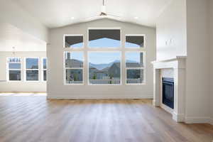 Unfurnished living room featuring a glass covered fireplace, light wood-type flooring, ceiling fan, vaulted ceiling, and a mountain view