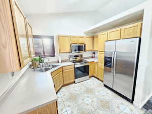 Kitchen featuring stainless steel appliances, light countertops, light brown cabinets, lofted ceiling, and light tile patterned flooring