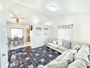 Living area featuring vaulted ceiling, a ceiling fan, a textured ceiling, and dark tile patterned floors