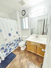 Bathroom with vanity, a shower with shower curtain, and light stone finish flooring