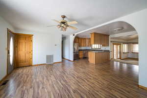 Kitchen with arched walkways, open floor plan, brown cabinets, dark wood-type flooring, and appliances with stainless steel finishes